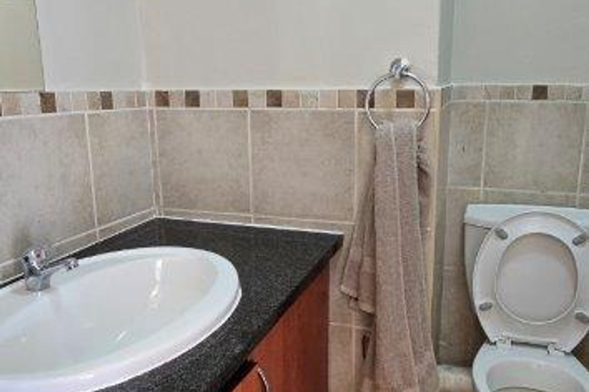 A functional bathroom featuring a vanity with granite countertop, drop-in sink, and standard toilet, finished with neutral wall and floor tiling.