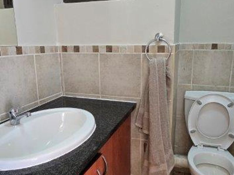 A functional bathroom featuring a vanity with granite countertop, drop-in sink, and standard toilet, finished with neutral wall and floor tiling.