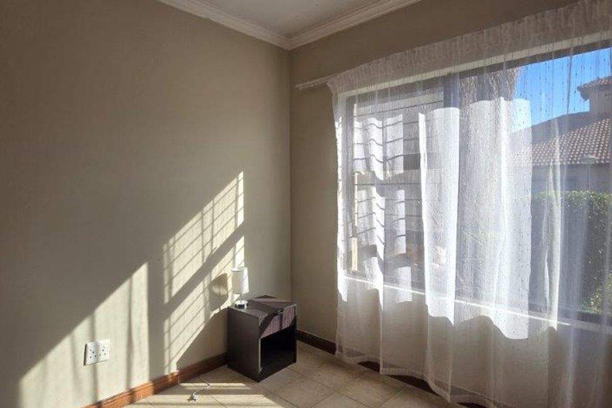 A bright, empty bedroom featuring tiled flooring, neutral walls, and a large window with natural light.
