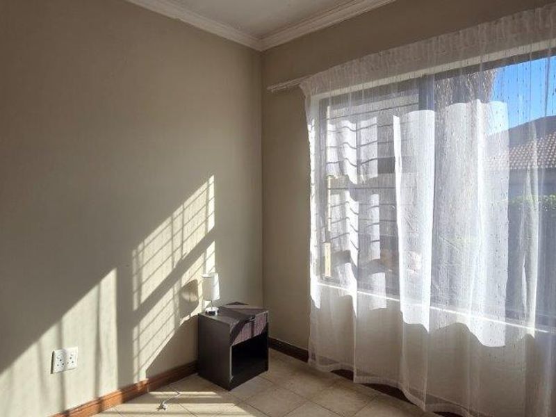 A bright, empty bedroom featuring tiled flooring, neutral walls, and a large window with natural light.