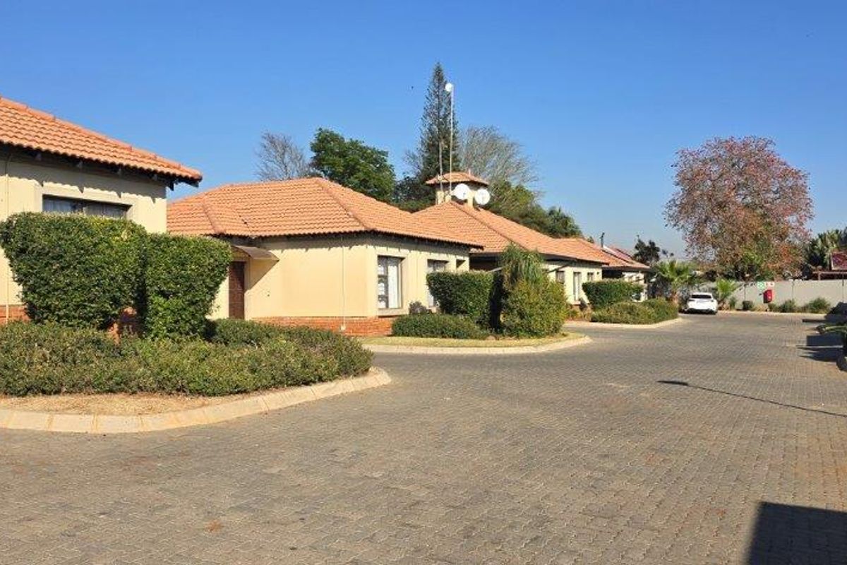 A view of the townhouse complex exterior featuring paved driveways, well-maintained garden beds, and traditional terracotta roof tiles.