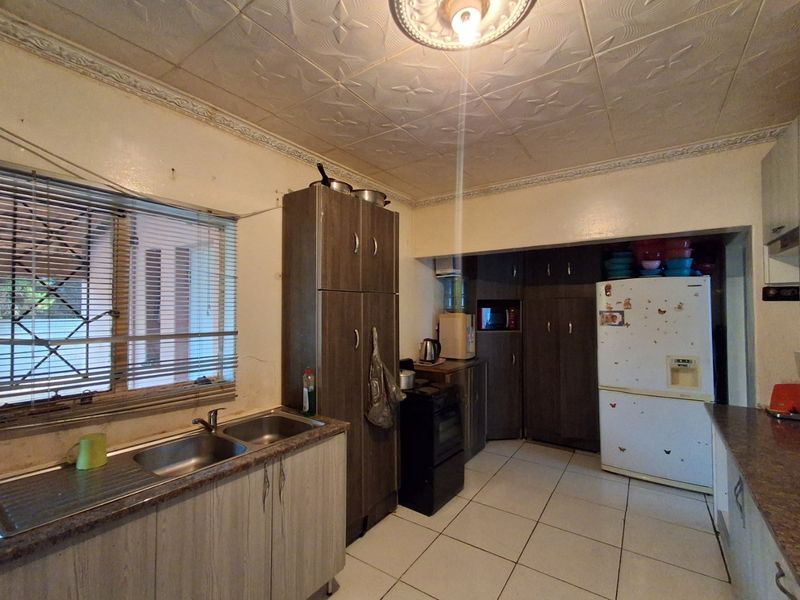 A functional kitchen featuring built-in cabinetry, double sink, laminate countertops, and tiled flooring, offering potential for modernization and aesthetic updates.