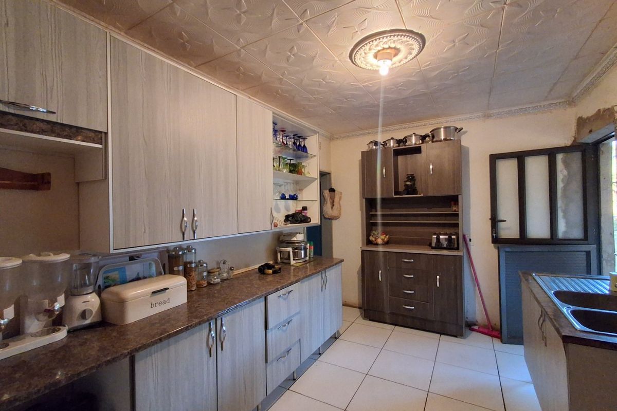 A functional kitchen featuring laminate cabinetry, tiled flooring, and decorative ceiling tiles, offering a practical layout with ample storage space.