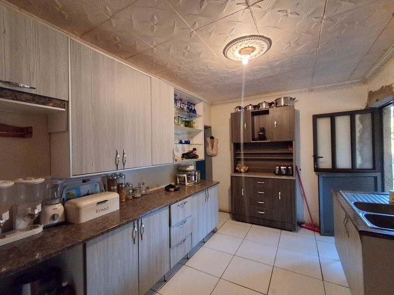 A functional kitchen featuring laminate cabinetry, tiled flooring, and decorative ceiling tiles, offering a practical layout with ample storage space.