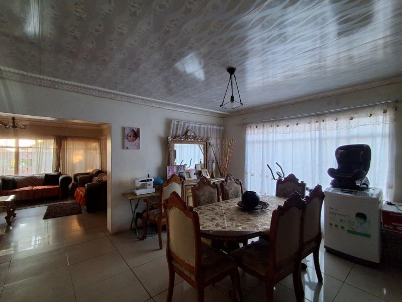 Open plan dining and living area featuring tiled flooring, decorative ceiling panels, and large windows allowing for natural light.