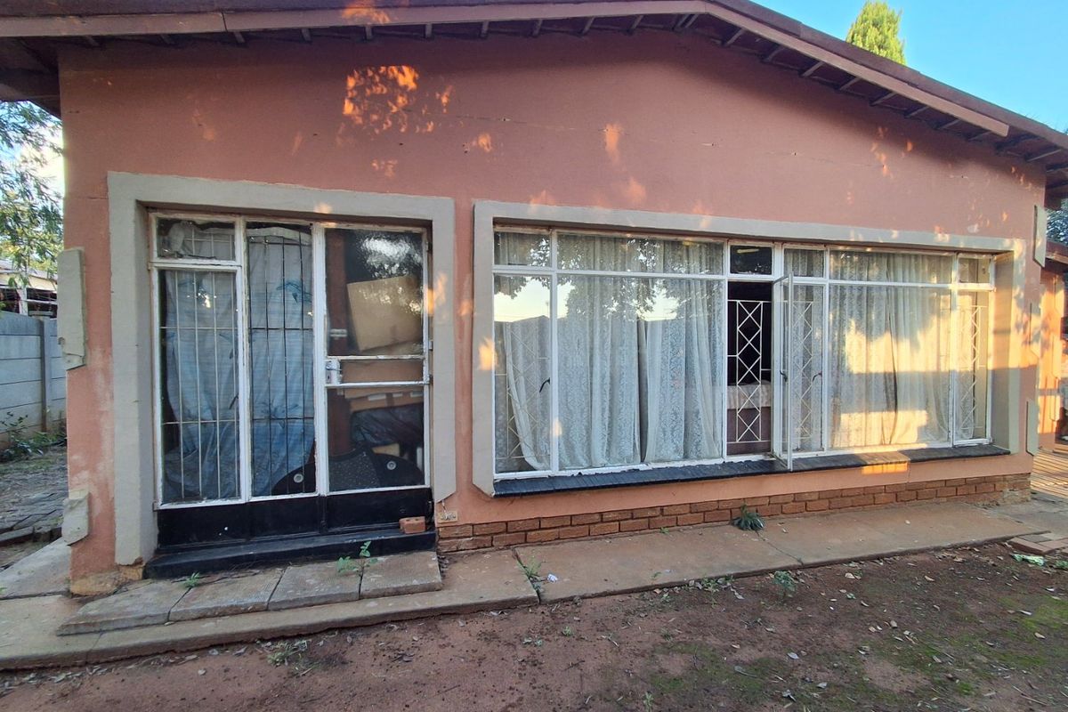 Rear exterior view of the house featuring large windows, metal security gates, and a concrete pathway requiring maintenance.