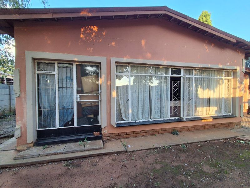 Rear exterior view of the house featuring large windows, metal security gates, and a concrete pathway requiring maintenance.