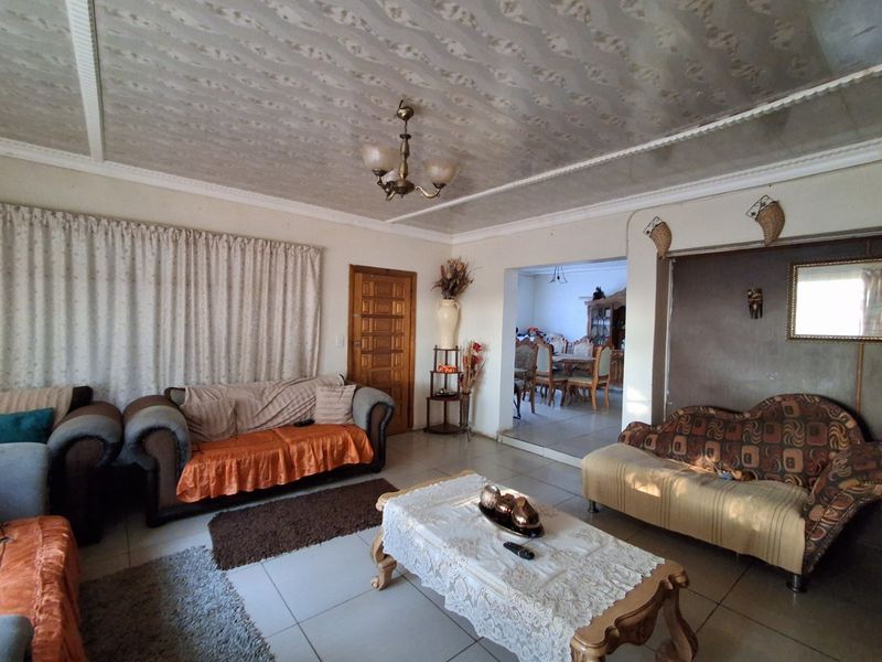 Spacious living room featuring tiled flooring, a textured ceiling with coving, and a central chandelier, with an open-plan flow into the adjacent dining area.