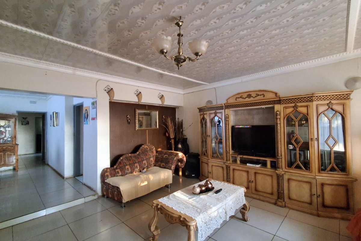 A spacious living room featuring tiled flooring, a decorative ceiling, and a large built-in wall unit, offering potential for modern updates.