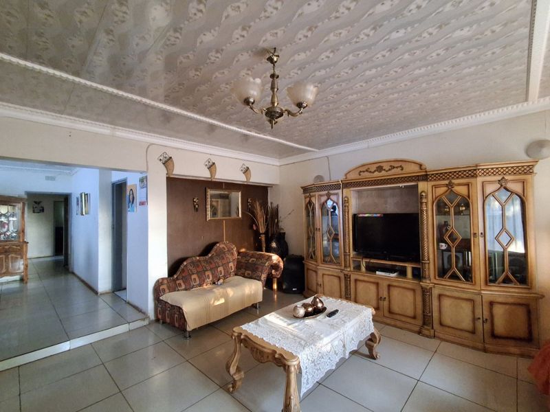 A spacious living room featuring tiled flooring, a decorative ceiling, and a large built-in wall unit, offering potential for modern updates.