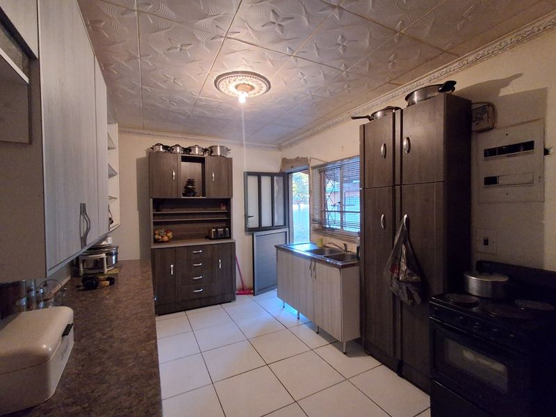 A functional kitchen featuring built-in cabinetry, laminate countertops, a double sink, and tiled flooring, with direct access to the exterior.
