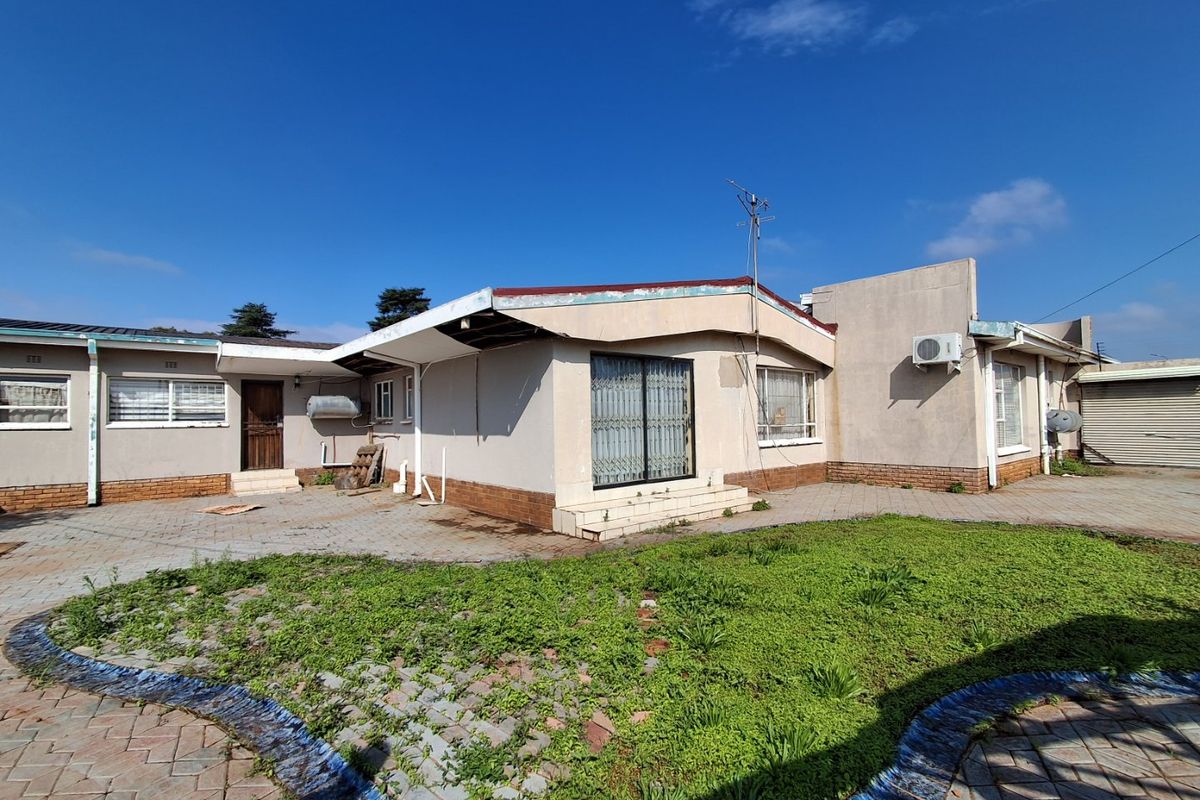 Rear exterior view of the house featuring a paved patio area, sliding glass doors, and an air conditioning unit, showing signs of exterior wear.