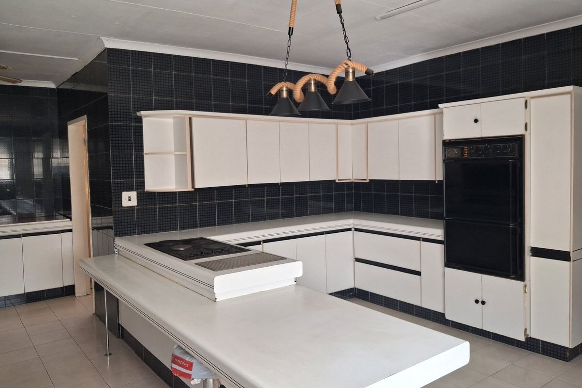 A spacious kitchen featuring white cabinetry, a built-in oven, a hob, and a large central island with a breakfast bar.