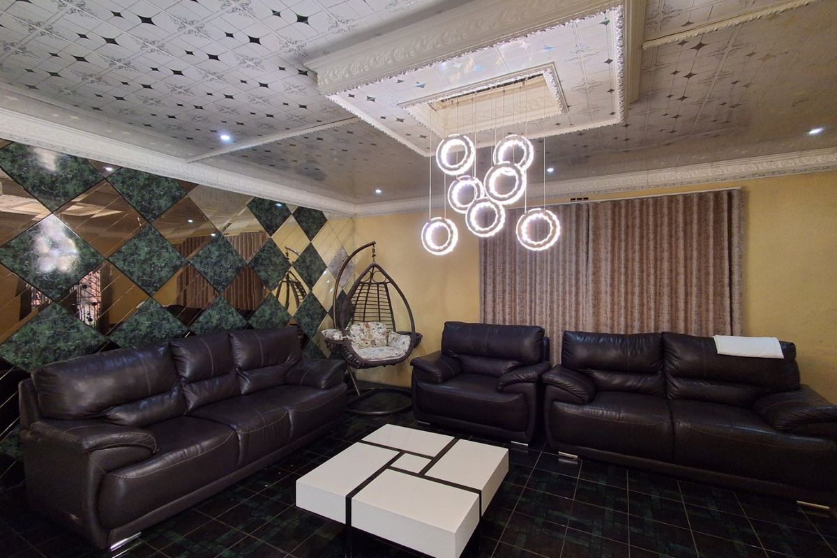 Spacious living room featuring a decorative coffered ceiling, mirrored wall accents, tiled flooring, and a contemporary circular pendant light fixture.