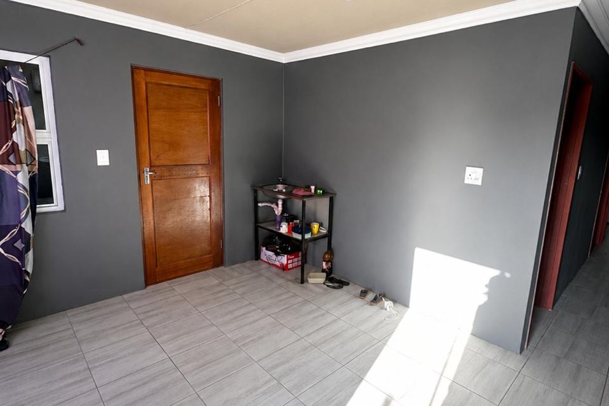 A bright, empty living area featuring modern grey floor tiles, dark grey walls, and a timber door, offering a clean canvas for interior design.