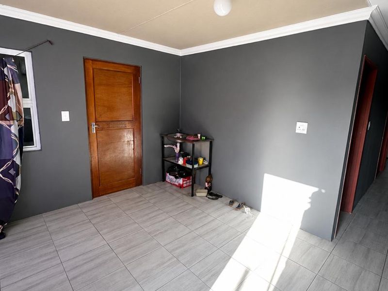 A bright, empty living area featuring modern grey floor tiles, dark grey walls, and a timber door, offering a clean canvas for interior design.