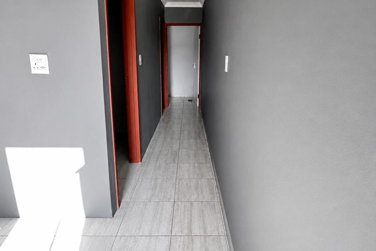 A clean, empty hallway featuring grey tiled flooring, neutral grey walls, and contrasting door frames, providing access to multiple rooms.