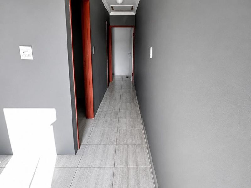 A clean, empty hallway featuring grey tiled flooring, neutral grey walls, and contrasting door frames, providing access to multiple rooms.