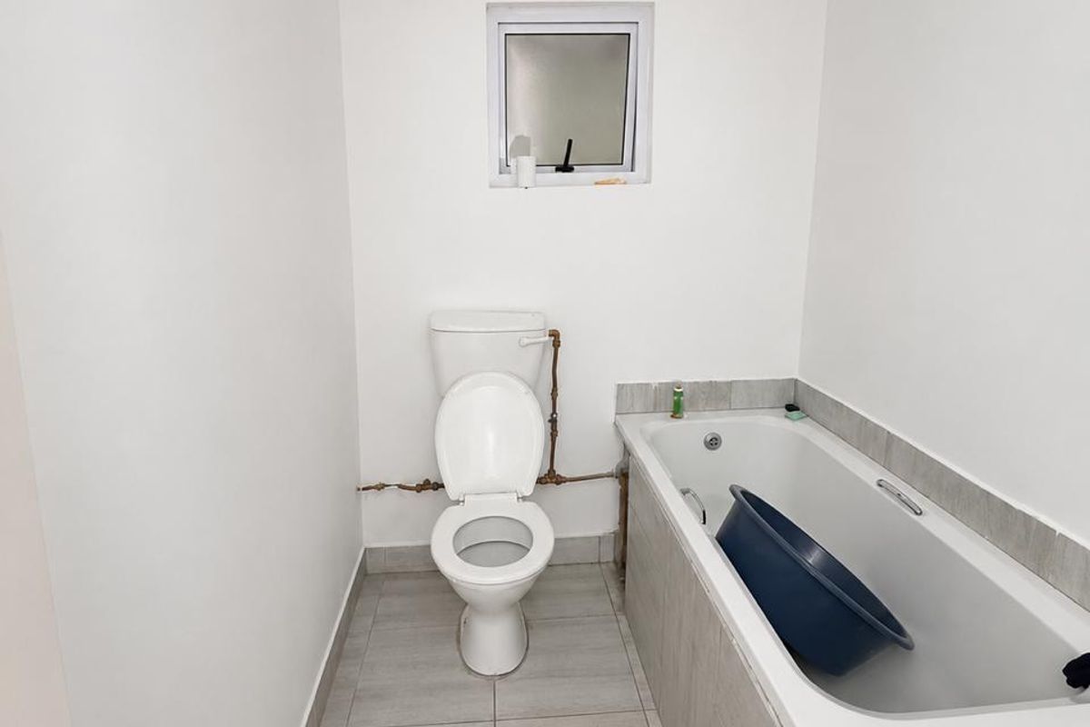 A functional bathroom featuring a standard toilet, a bathtub with tiled surround, and neutral floor tiling.