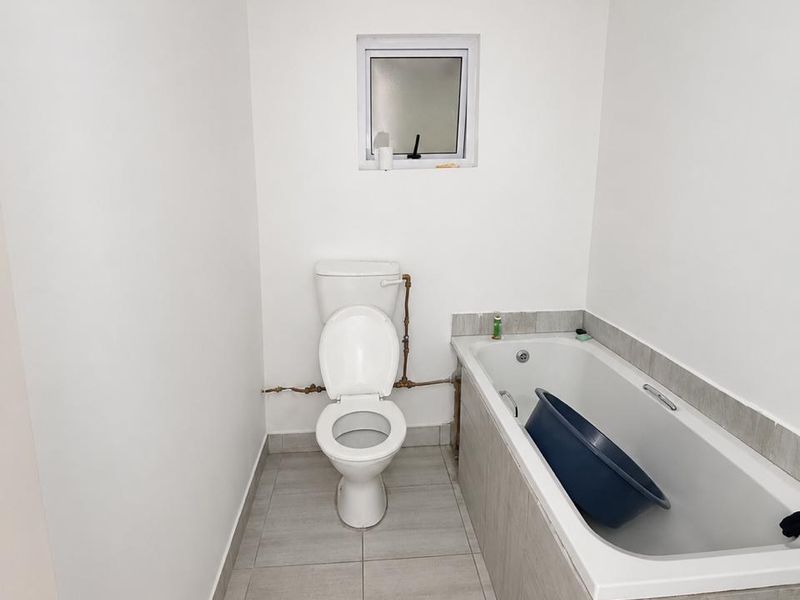 A functional bathroom featuring a standard toilet, a bathtub with tiled surround, and neutral floor tiling.