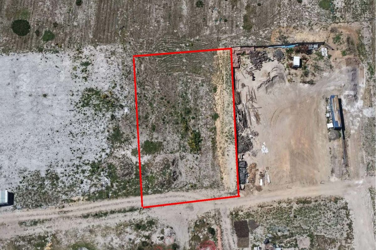 Aerial view of a vacant residential plot of land with a red boundary outline, featuring direct access to an unpaved road.
