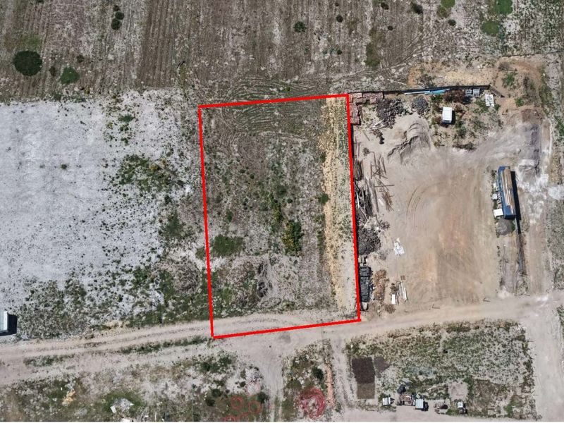 Aerial view of a vacant residential plot of land with a red boundary outline, featuring direct access to an unpaved road.