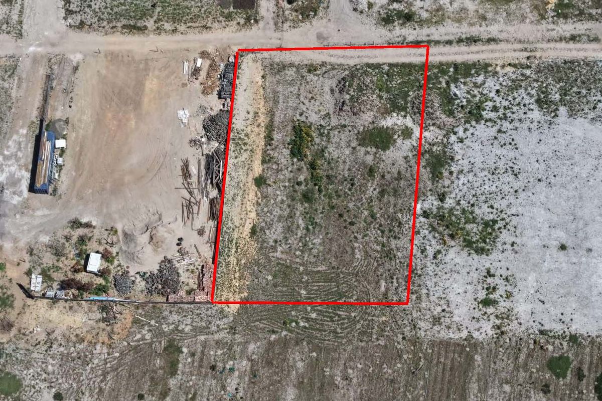 Aerial view of a vacant residential plot outlined in red, featuring natural ground cover and access to an unpaved road.