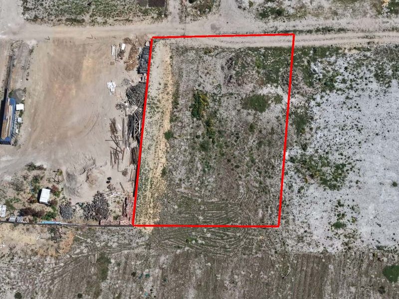 Aerial view of a vacant residential plot outlined in red, featuring natural ground cover and access to an unpaved road.