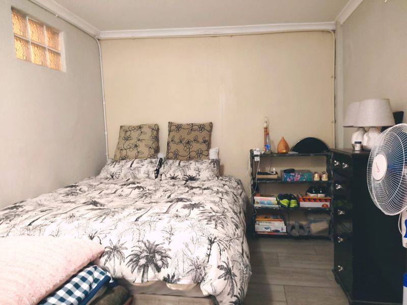 A compact bedroom featuring laminate flooring, a small glass block window, and visible surface-mounted electrical conduit along the wall.