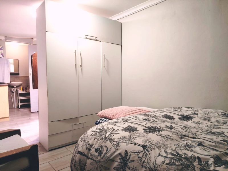 A bedroom featuring a built-in wardrobe and tiled flooring, with an adjacent view into a bathroom area.