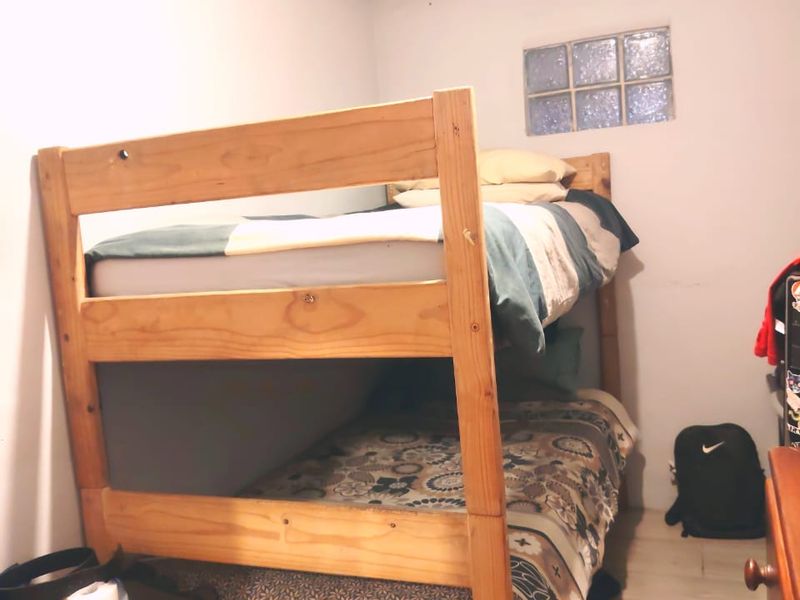 A compact bedroom featuring tiled flooring and a small glass block window, showing signs of ceiling water damage.