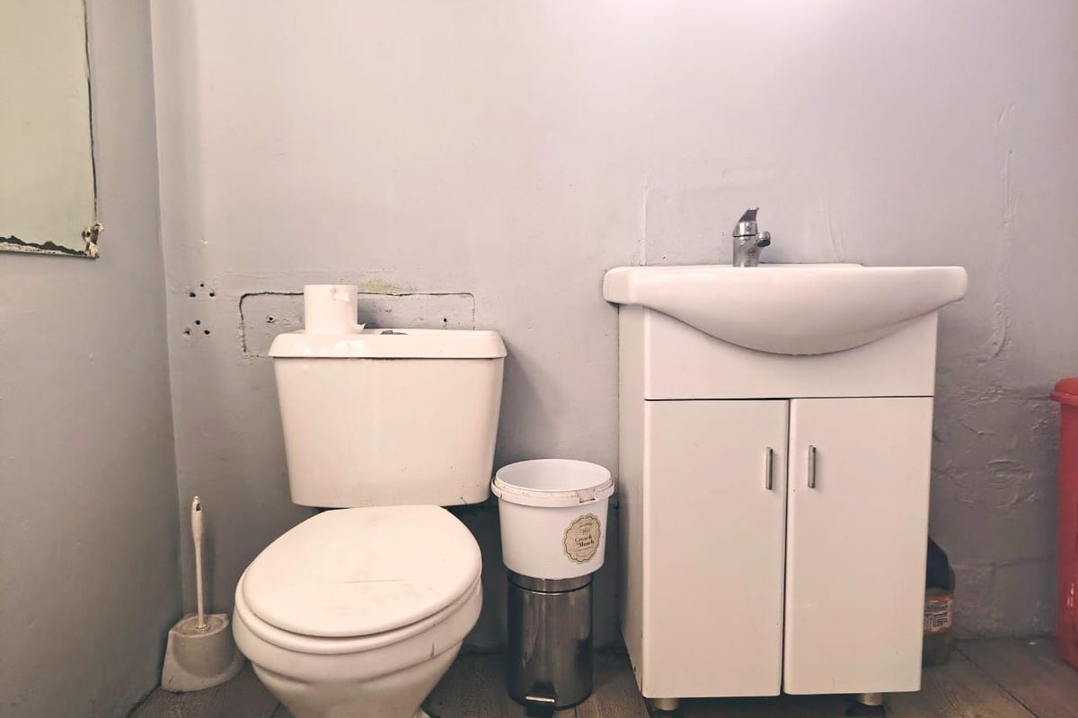 A small bathroom featuring a standard toilet and a vanity unit with a washbasin, showing signs of wear on the wall surfaces.