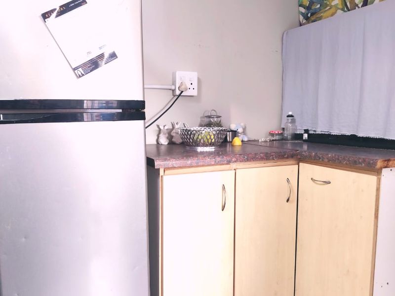 A compact kitchen corner featuring light-toned laminate cabinetry, a durable countertop, and a functional electrical outlet, showing signs of age and wear.