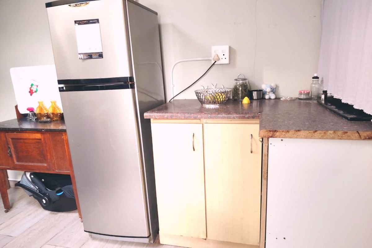 A compact kitchen area featuring laminate countertops and basic base cabinetry, showing signs of wear and minor wall damage.