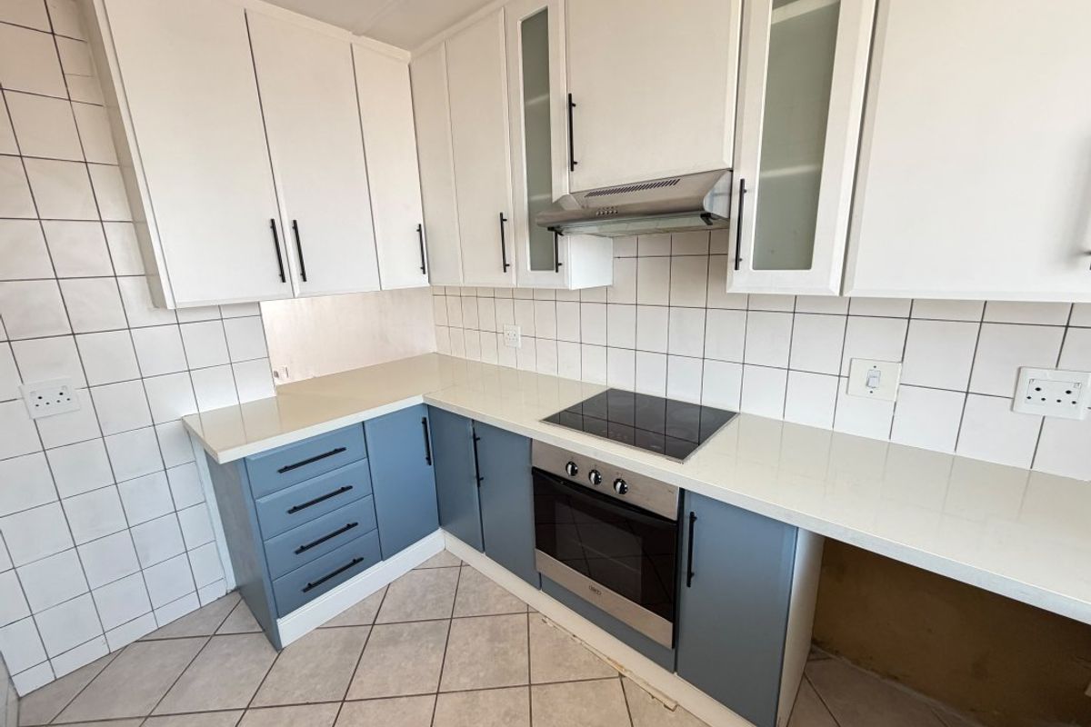 A clean, modern kitchen featuring two-tone cabinetry, quartz countertops, a built-in oven, and an electric hob with a tiled backsplash.