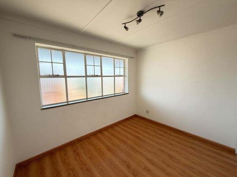 An empty bedroom featuring laminate flooring, a multi-pane window, and ceiling-mounted track lighting, providing a clean and neutral space ready for personalization.