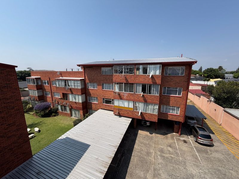 Aerial view of a multi-story brick apartment complex featuring a communal garden, paved parking area, and covered carports.