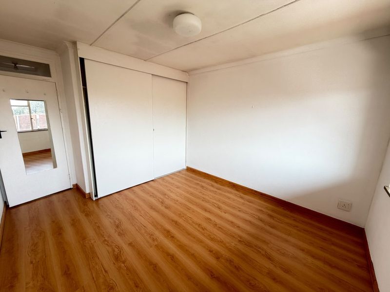 An empty bedroom featuring laminate flooring, a built-in sliding door wardrobe, and a neutral interior finish.