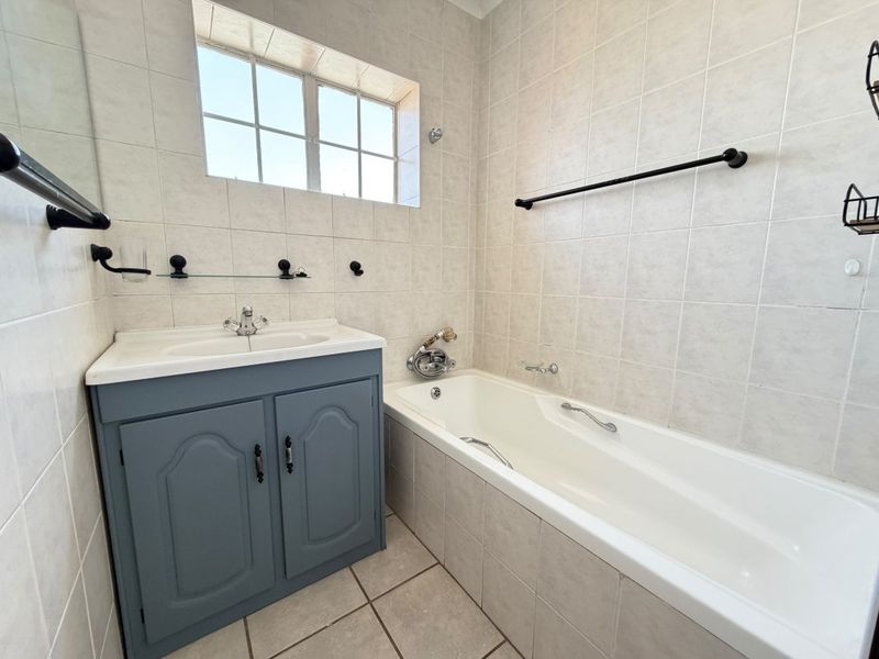 A clean, functional bathroom featuring a vanity cabinet, bathtub, and neutral wall tiling with modern black hardware accents.
