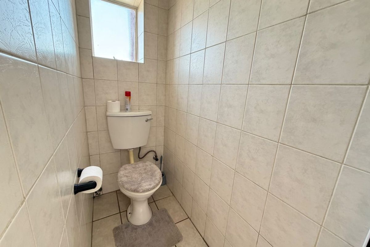 A compact guest toilet featuring full-height ceramic wall tiling and tiled flooring, requiring cosmetic updates to modernize the space.