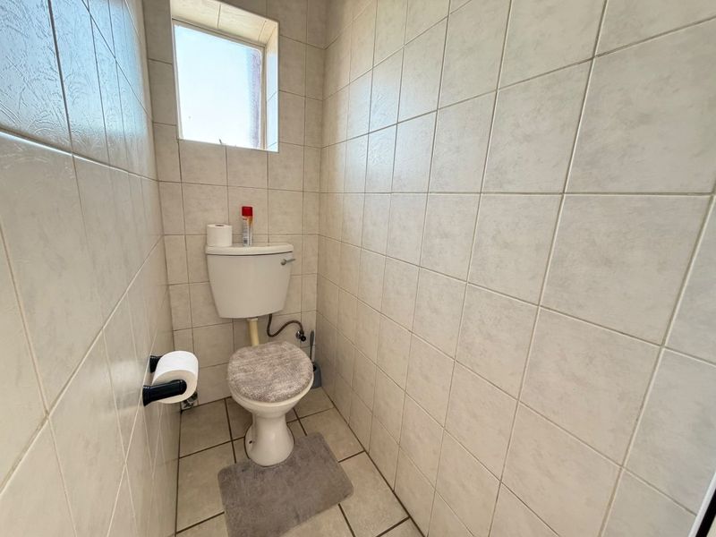 A compact guest toilet featuring full-height ceramic wall tiling and tiled flooring, requiring cosmetic updates to modernize the space.