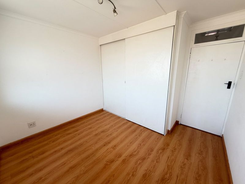 An empty bedroom featuring laminate flooring, a built-in sliding door wardrobe, and a door with a transom window.