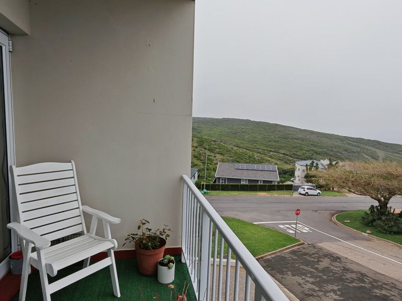 A balcony featuring a metal balustrade and sliding glass door access, offering an elevated view of the surrounding neighborhood and hillside.