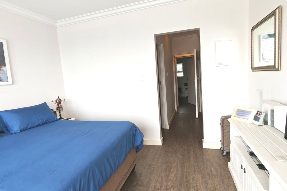 A well-maintained bedroom featuring laminate flooring, crown molding, and neutral wall finishes, with a doorway leading to an adjacent hallway.