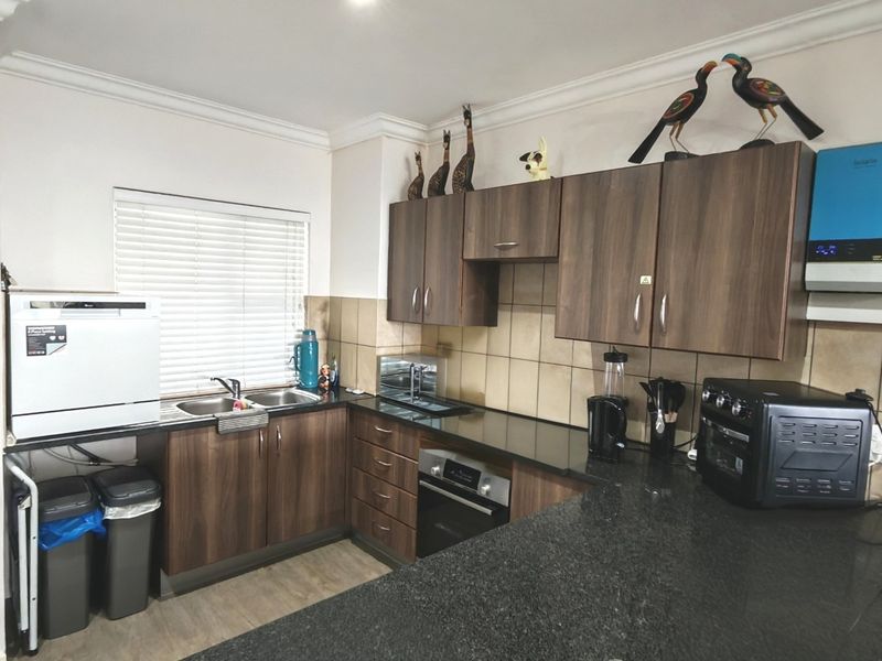 A functional kitchen featuring dark wood cabinetry, granite countertops, a double sink, built-in oven, and a tiled backsplash with an integrated inverter system.
