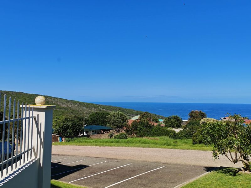 A clear elevated view of the ocean and surrounding coastal landscape, featuring a paved parking area and perimeter fencing in the foreground.