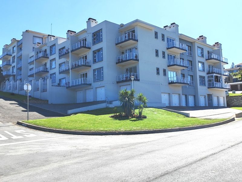 Exterior view of a multi-story apartment complex featuring private balconies, ground-level garage access, and a well-maintained landscaped lawn area.