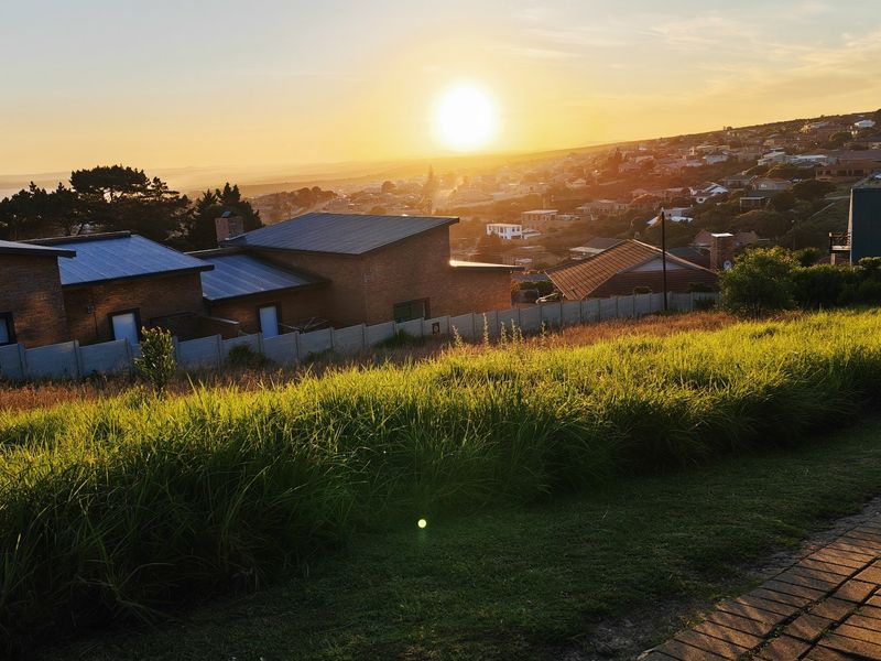 A scenic elevated view overlooking the surrounding residential neighborhood and coastline at sunset, captured from the vacant residential land.