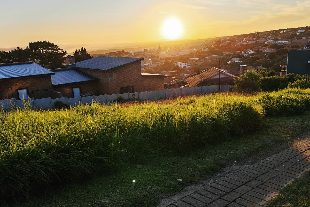 A scenic view overlooking a residential neighborhood at sunset, featuring a paved walkway and boundary wall on a vacant residential plot.