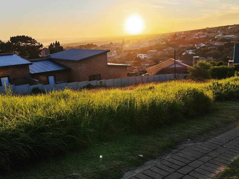 A scenic view overlooking a residential neighborhood at sunset, featuring a paved walkway and boundary wall on a vacant residential plot.